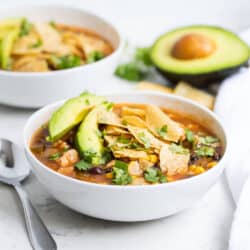 bowl of chicken tortilla soup with sliced avocado and crushed tortilla chips