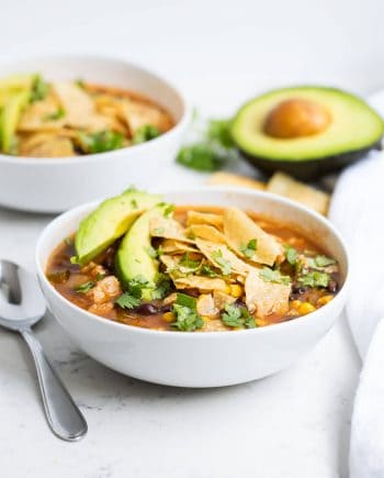 bowl of chicken tortilla soup with sliced avocado and crushed tortilla chips