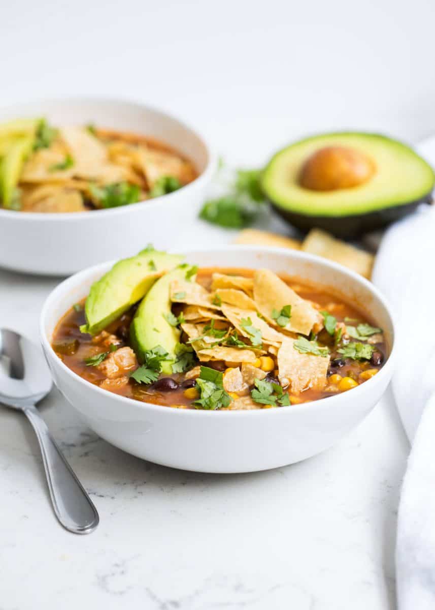 bowl of chicken tortilla soup with sliced avocado and crushed tortilla chips