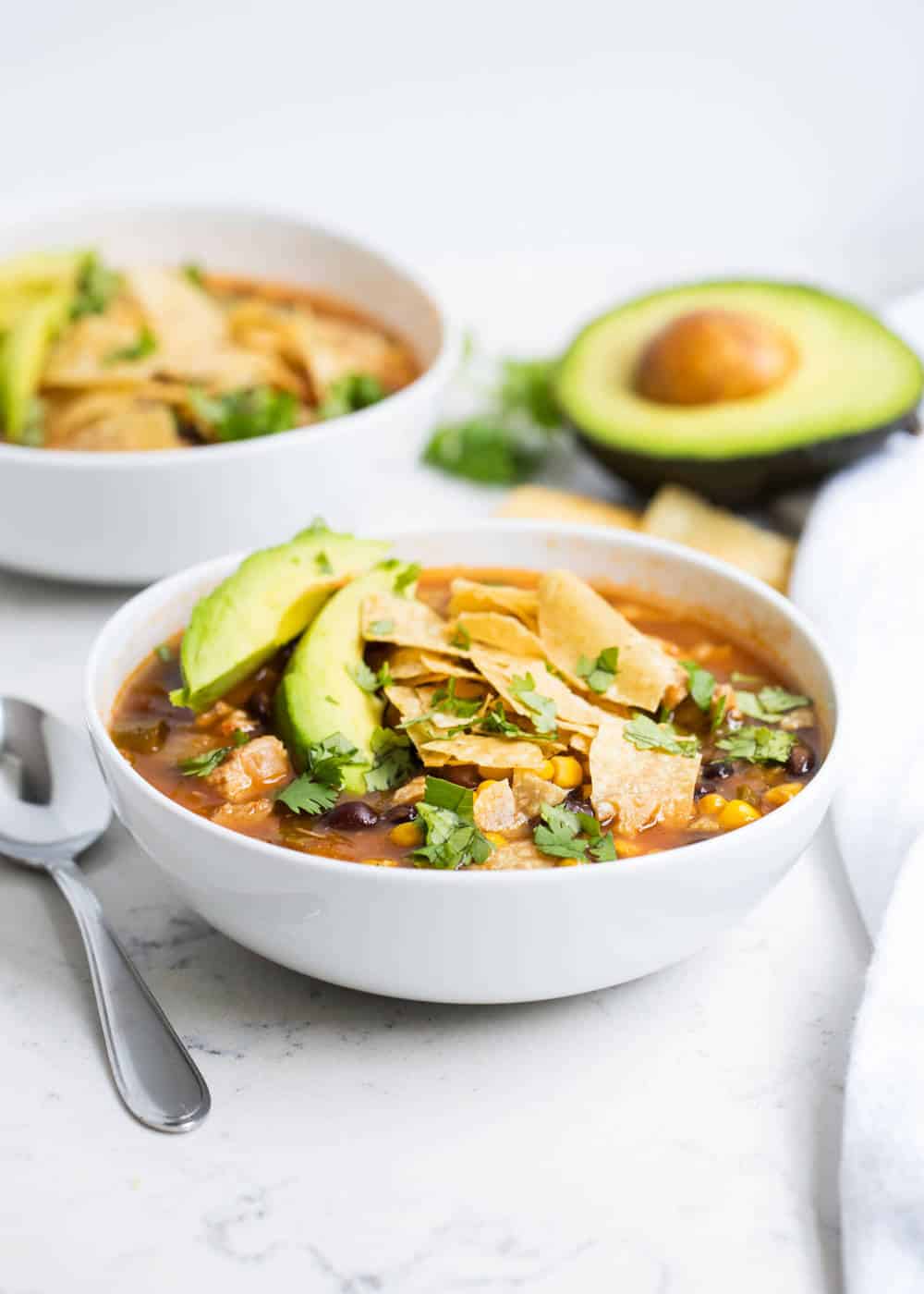 bowl of chicken tortilla soup with sliced avocado and crushed tortilla chips 