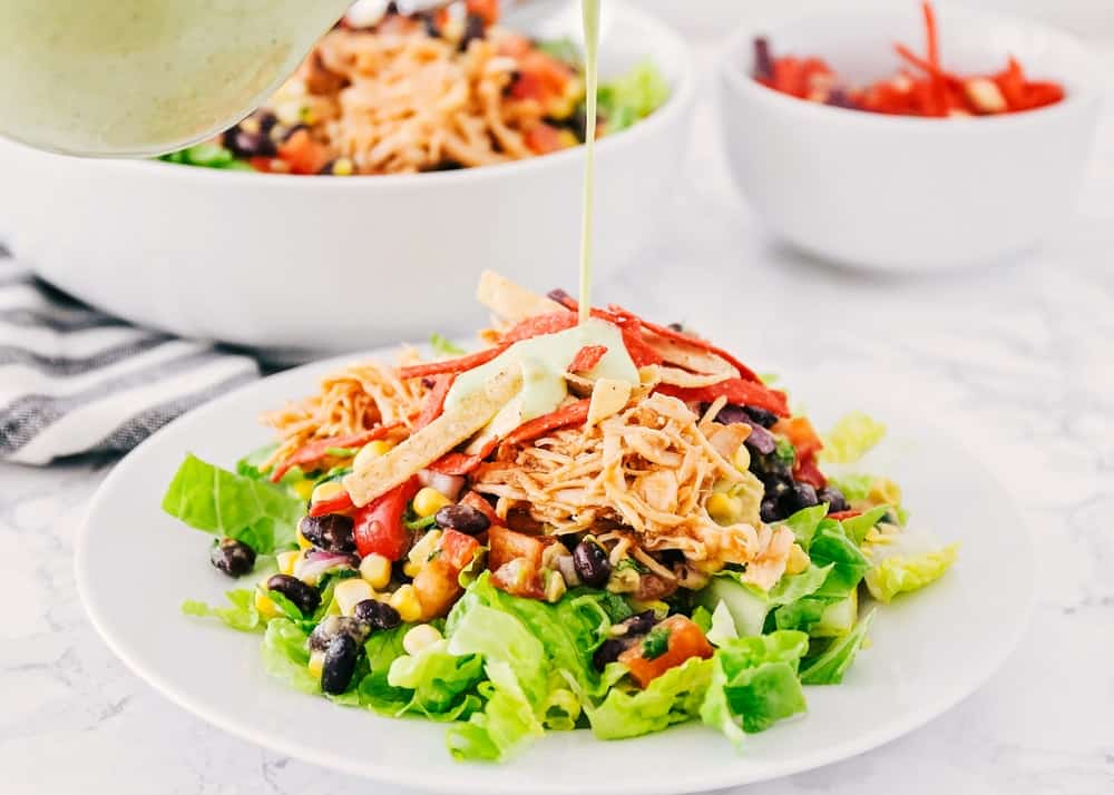 Pouring cilantro lime dressing on top of bbq chicken salad.