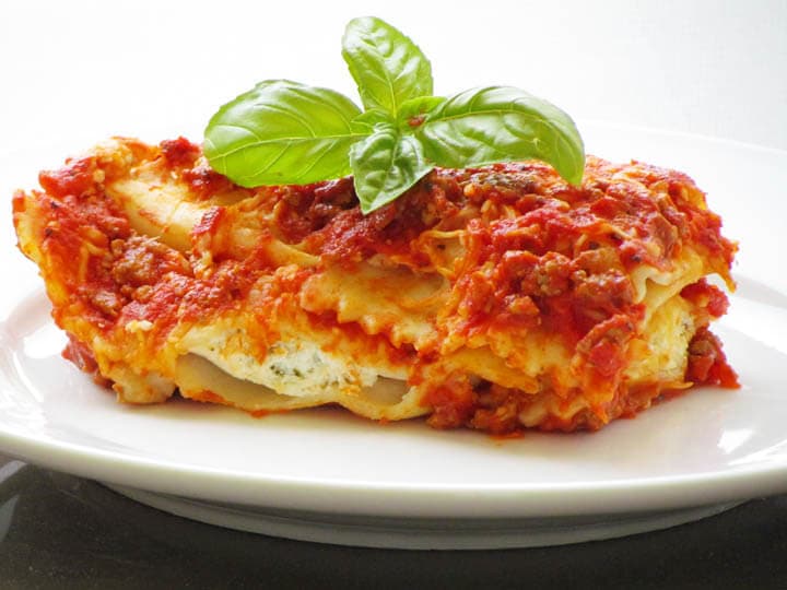 Piece of baked beef ravioli on a plate with fresh basil on top.