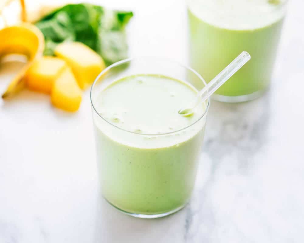 green smoothie in a clear glass with a straw 