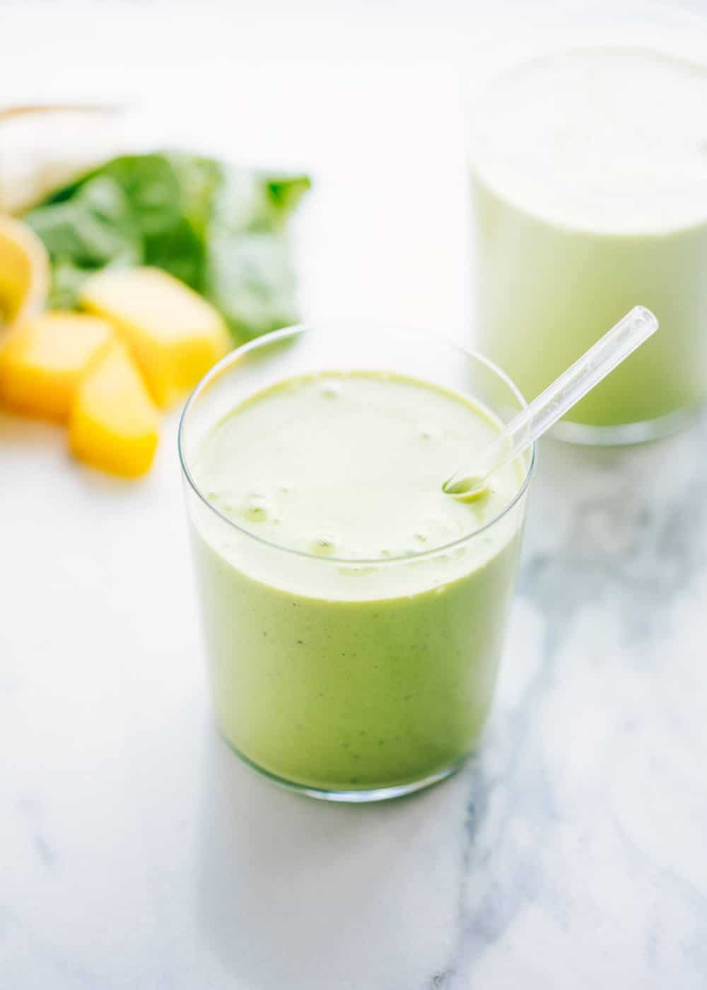 Healthy green smoothie recipe in a glass with a straw.
