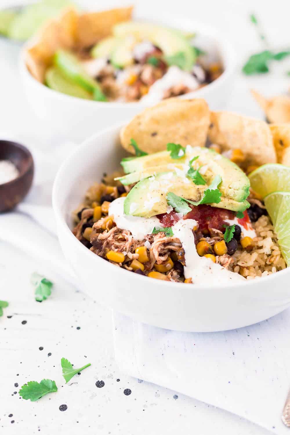 Chicken taco bowl topped with sliced avocado, limes and tortilla chips.