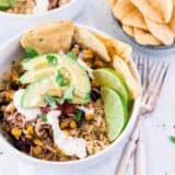 chicken taco bowl topped with sliced avocado, sour cream, cilantro, fresh limes and tortilla chips
