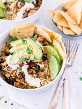 chicken taco bowl topped with sliced avocado, sour cream, cilantro, fresh limes and tortilla chips