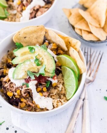 chicken taco bowl topped with sliced avocado, sour cream, cilantro, fresh limes and tortilla chips