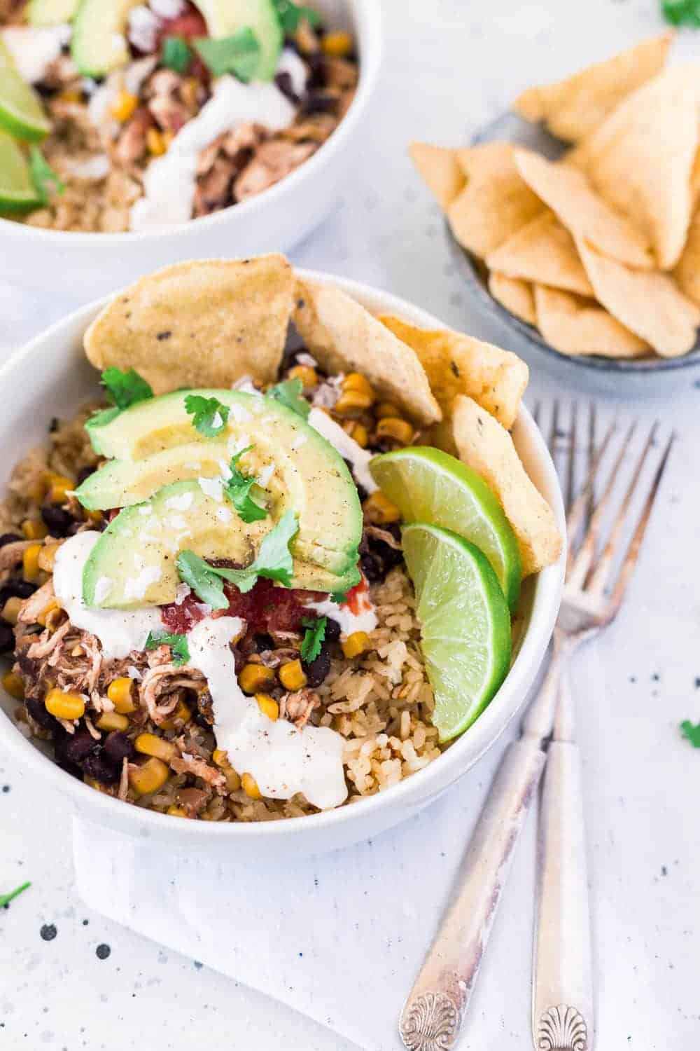 Chicken taco bowl topped with sliced avocado, sour cream, cilantro, fresh limes and tortilla chips.