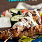 grilled chicken skewers on top of salad with tzatziki sauce