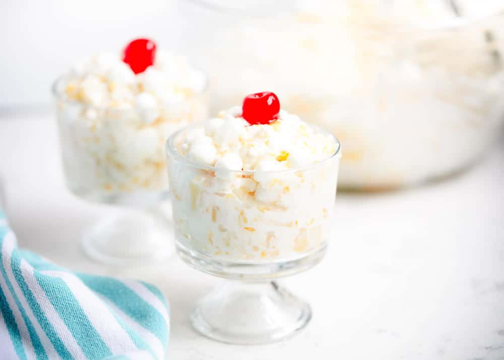 Ambrosia salad in a trifle dish with a cherry on top.