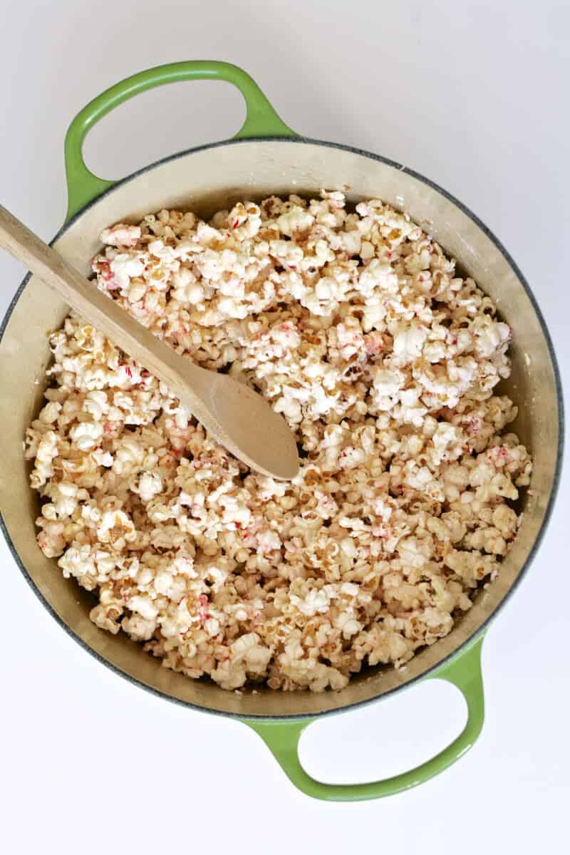 mixing together candy cane popcorn with a wooden spoon 