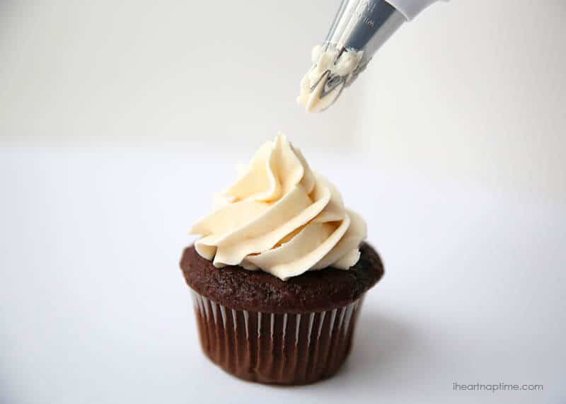 Piping frosting onto a chocolate cupcake.