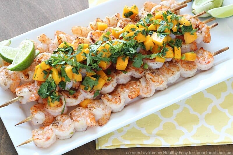 grilled shrimp skewers on a serving tray topped with mango salsa 