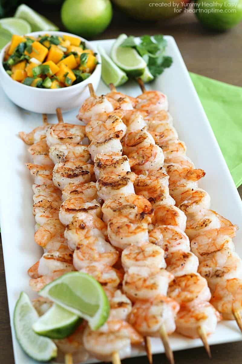plate of grilled shrimp skewers with fresh limes and mango salsa on the side 