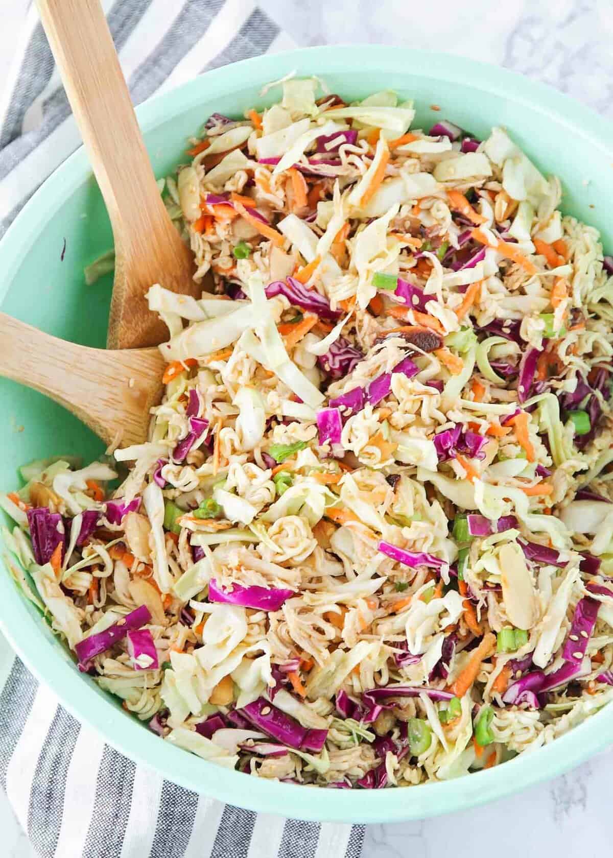 Ramen noodle cabbage salad in a green bowl with wooden spoons.