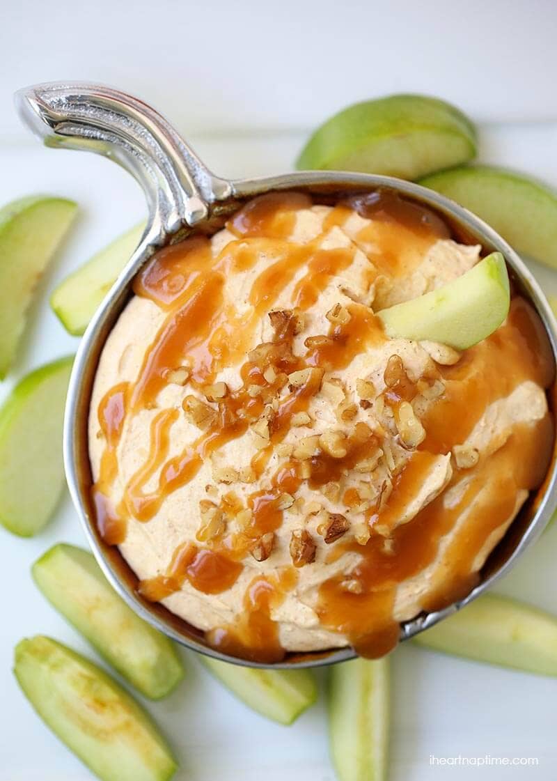 Easy pumpkin cheesecake dip in a silver bowl with apple slices and a caramel drizzle.