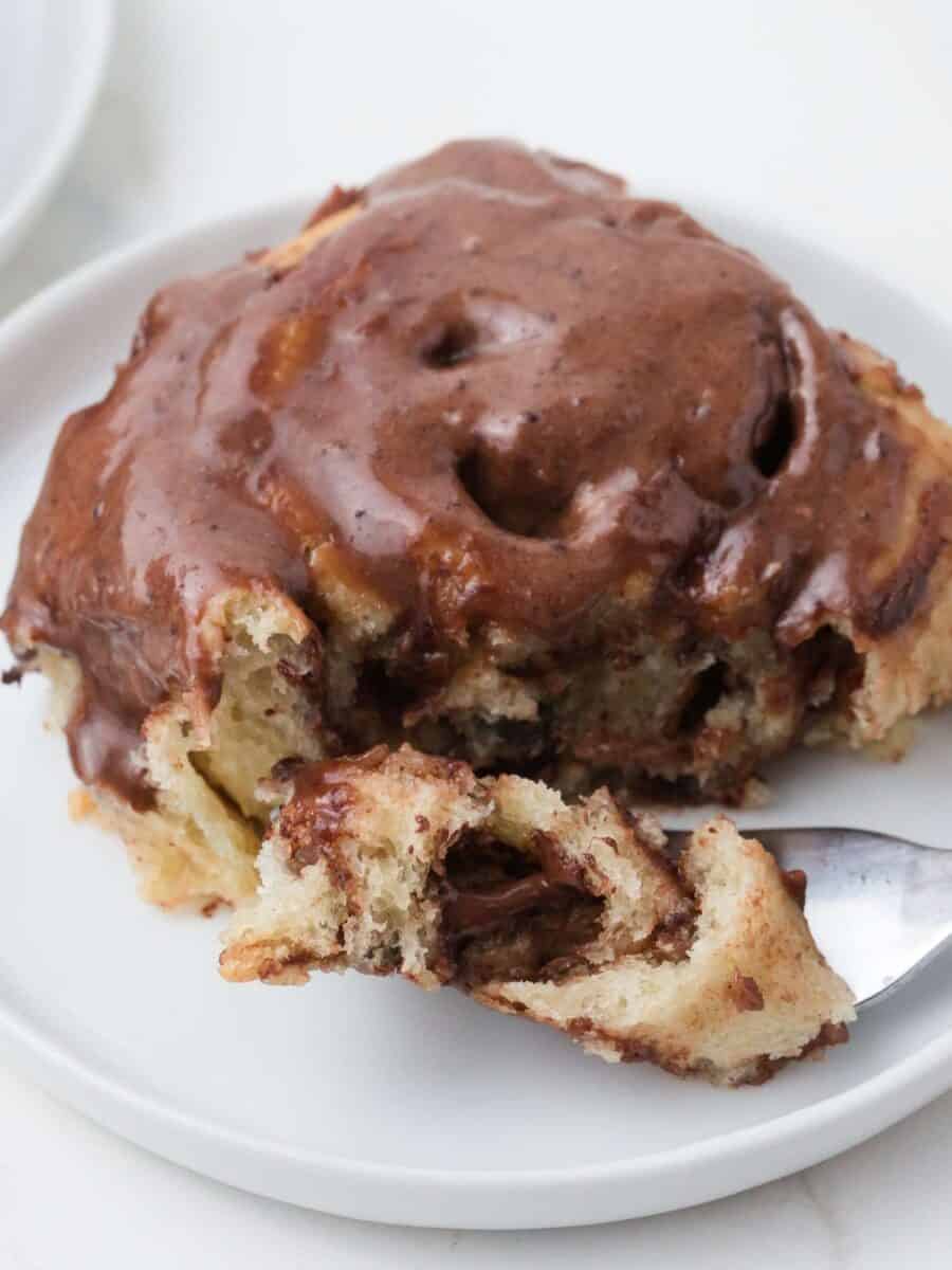 Close up of chocolate cinnamon roll on white plate with fork.