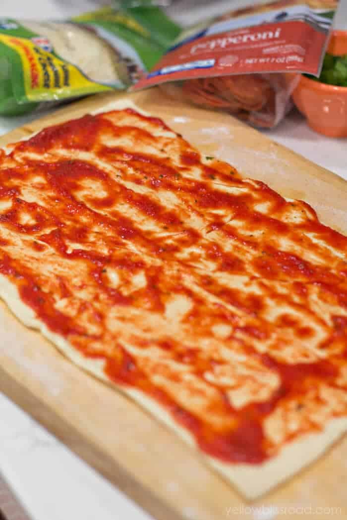 Ausgerollter Pizzateig mit Sauce darauf