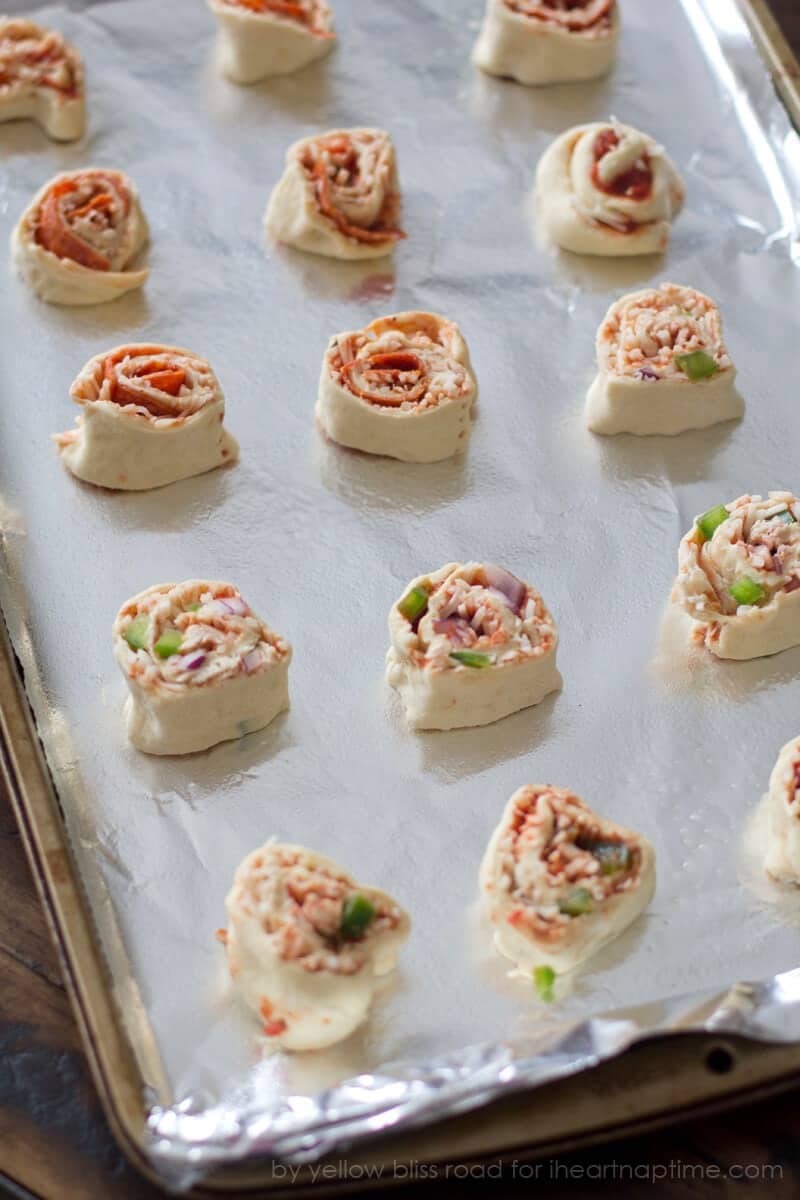 Uncooked pizza pinwheel rolls on a foil-lined baking sheet.