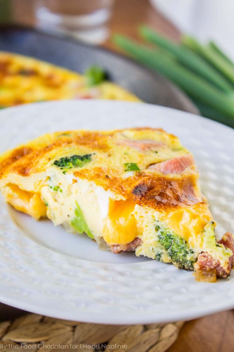 Slice of cheesy ham and broccoli frittata on a white plate.
