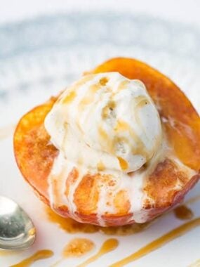 Close-up of baked peach half topped with melting vanilla ice cream and drizzled with caramel.