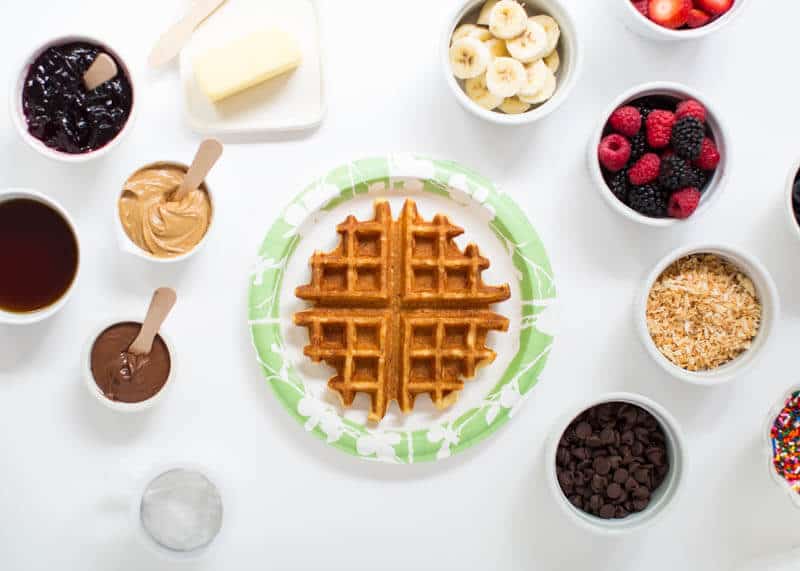 Waffle on a paper plate with toppings on the counter.