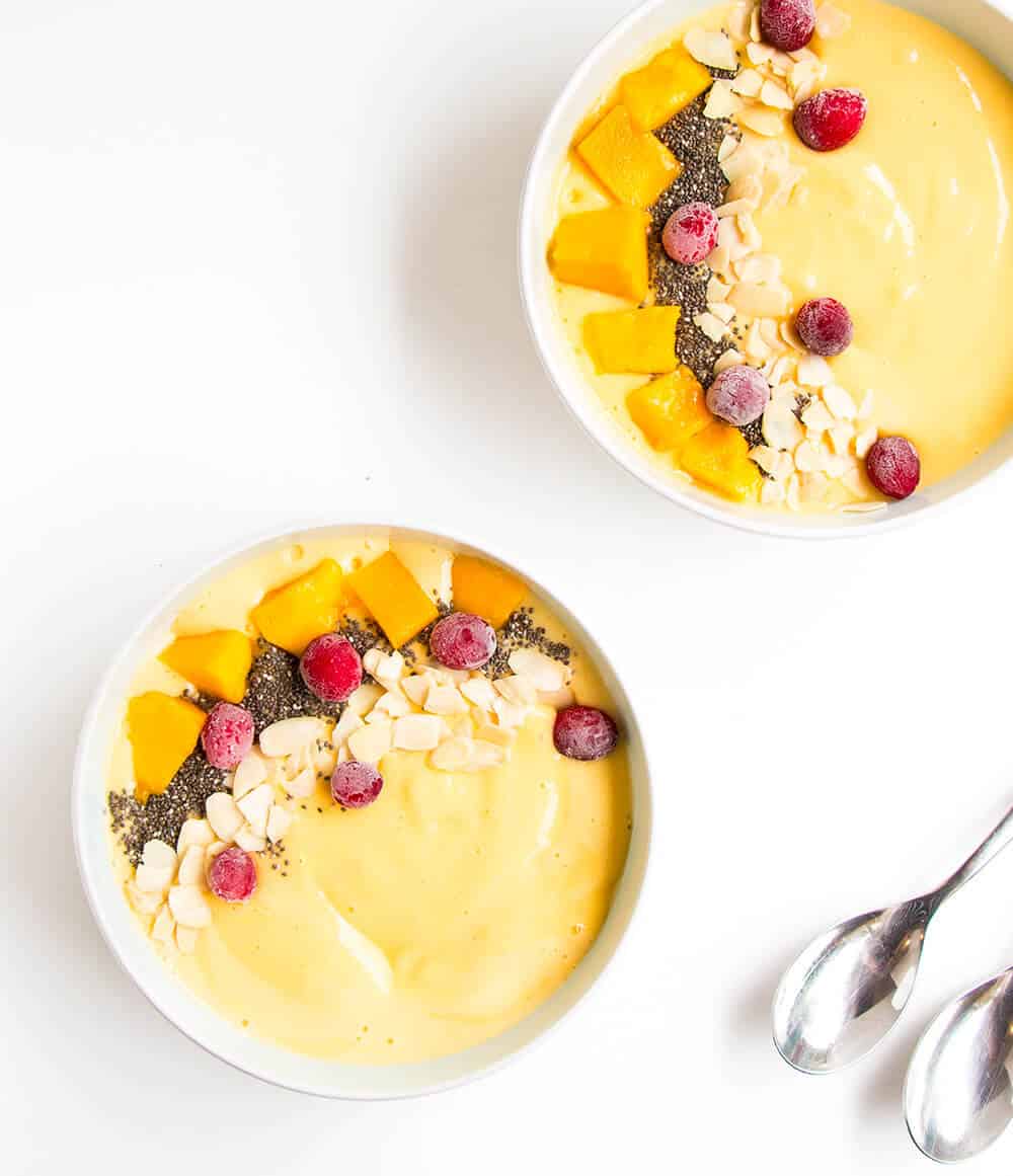 Two mango smoothie bowls with spoons.