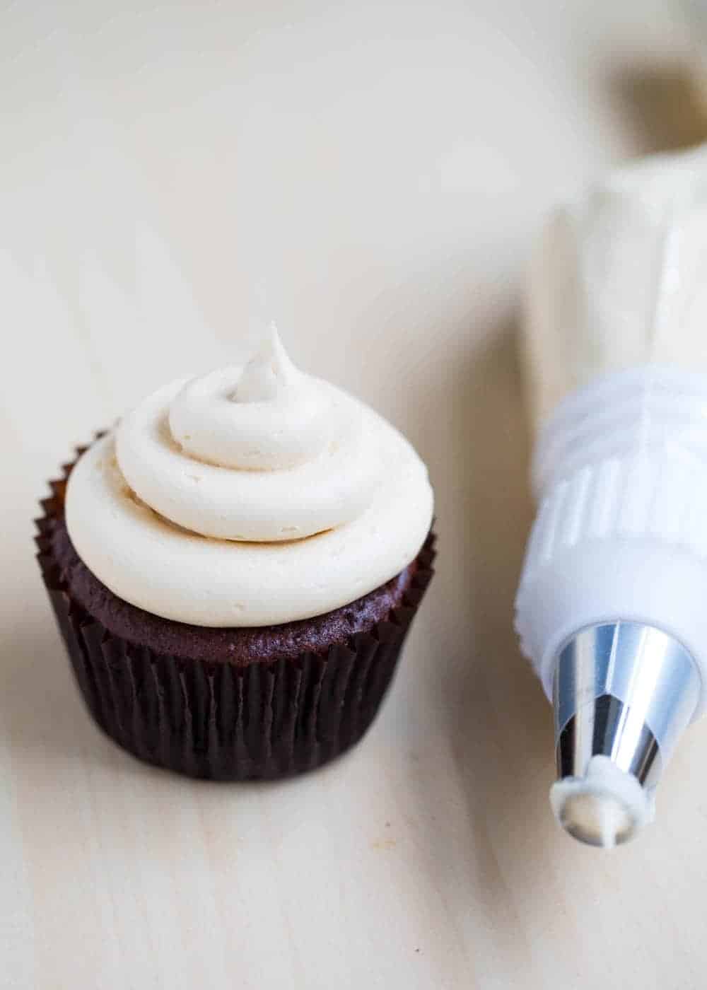 Piping a chocolate cupcake with a piping tip.