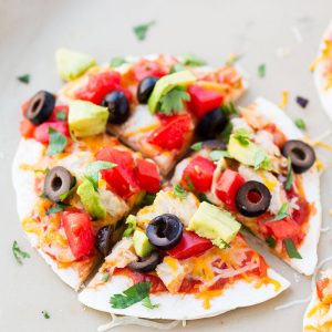 15-Minute Mexican Pizza Recipe - a dish the whole family will love! Warm tortillas stuffed with refried beans, meat, melt-y cheese and topped with salsa, tomatoes, cilantro, avocado and olives.