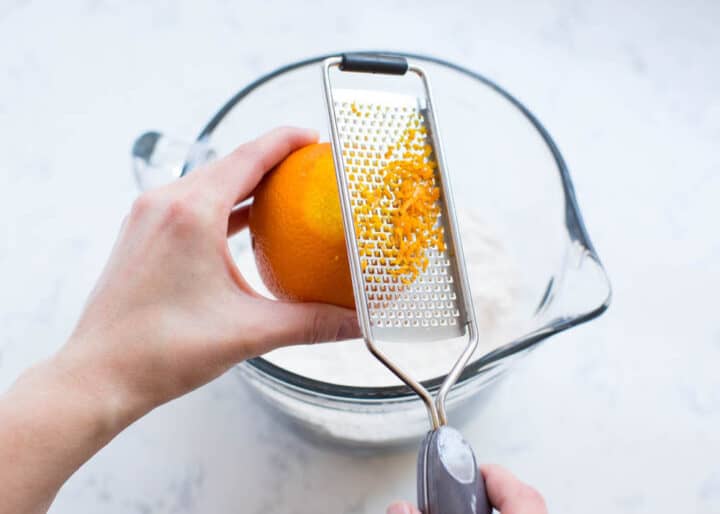 zesting an orange into a glass measuring cup 