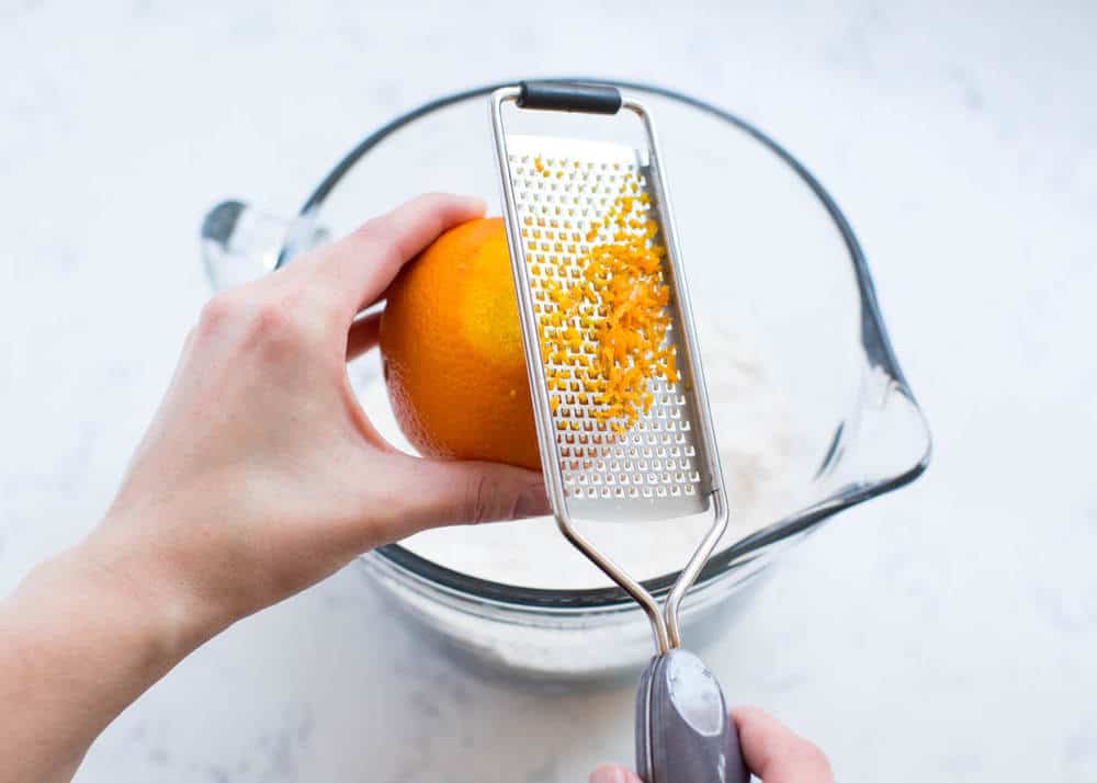 Zesting an orange into a glass measuring cup.