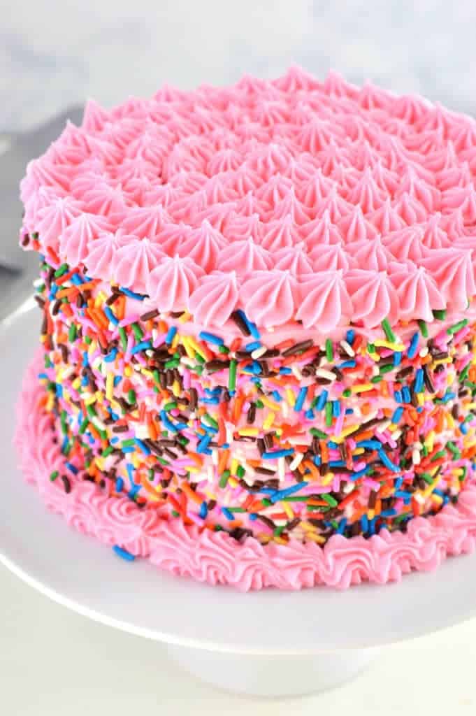 A close up of a pink cake with sprinkles 