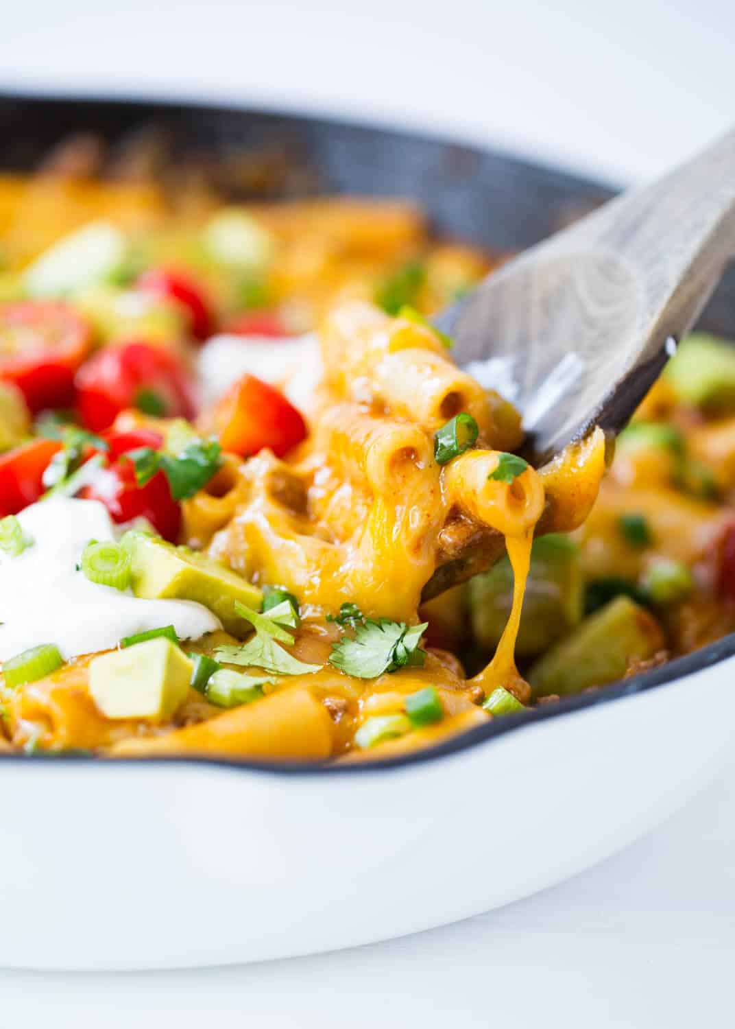 Scooping out cheesy enchilada pasta with a wooden spoon.