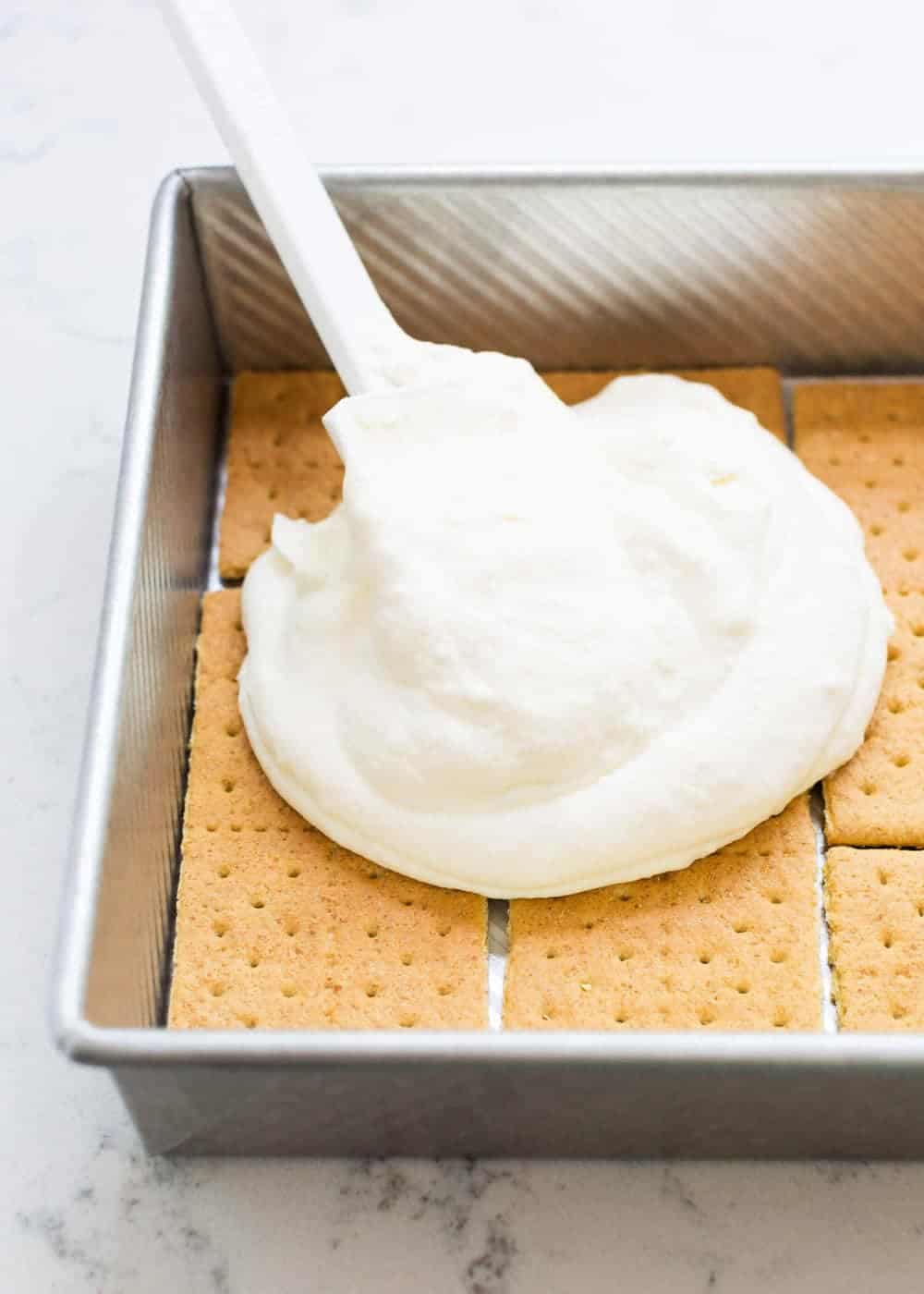 Spreading whipped cream over graham crackers in pan.