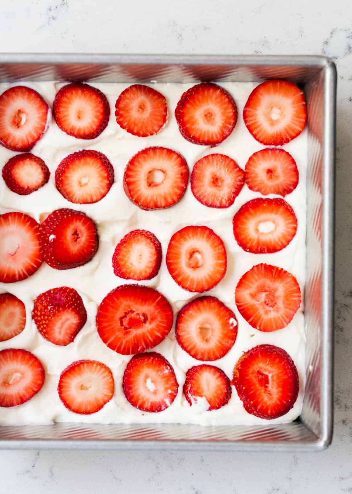 Sliced strawberries on top of whipped cream in pan.