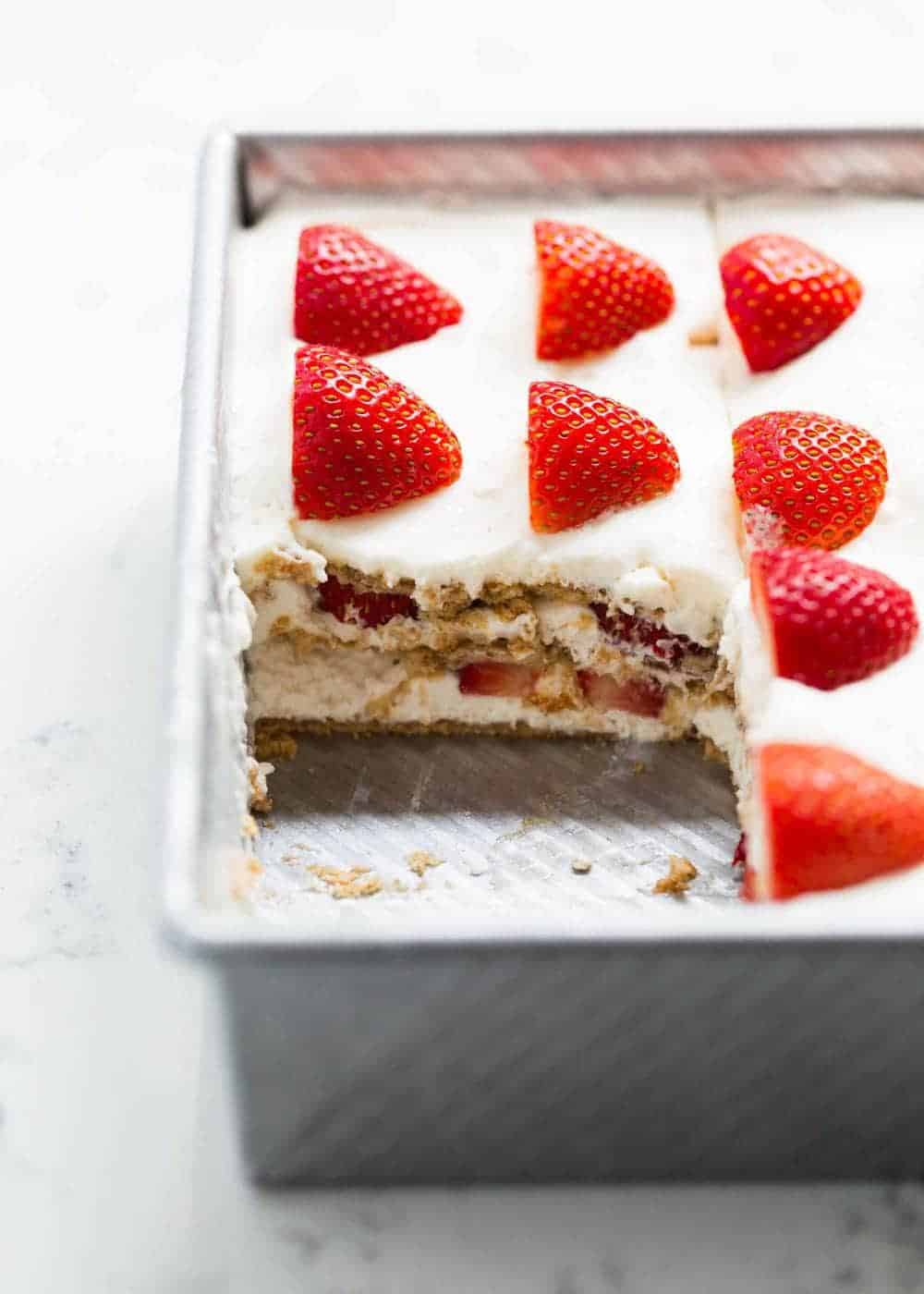 Strawberry icebox cake in pan with slice taken out.