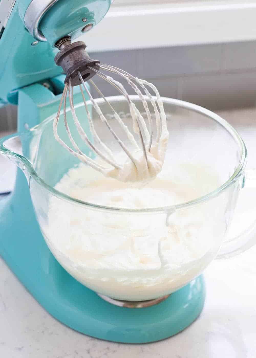 Homemade whipped cream in a blue kitchen aid mixer.
