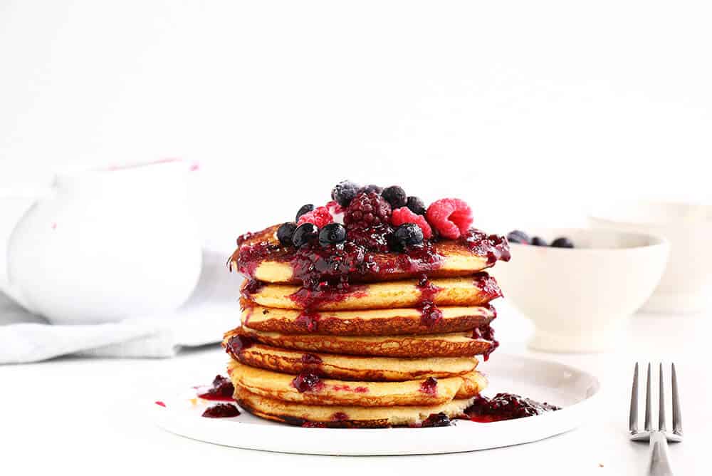 stack of pancakes topped with berries on a white plate 