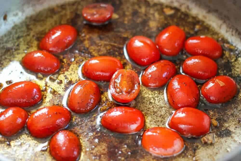 Tomatoes frying in bacon grease on skillet.