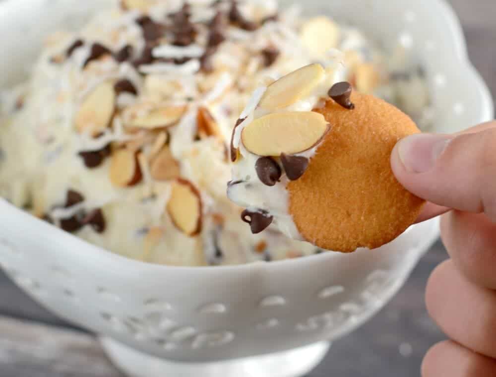 dipping a vanilla wafer into a bowl of almond joy dip 