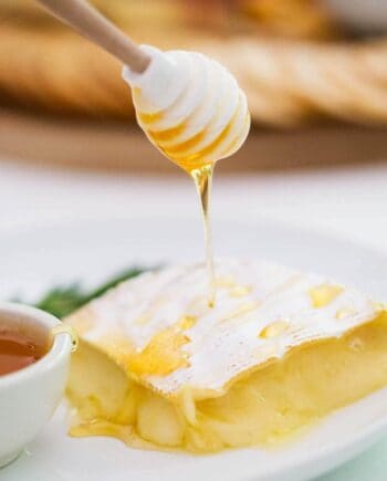 drizzling honey onto baked brie with a honey dipper