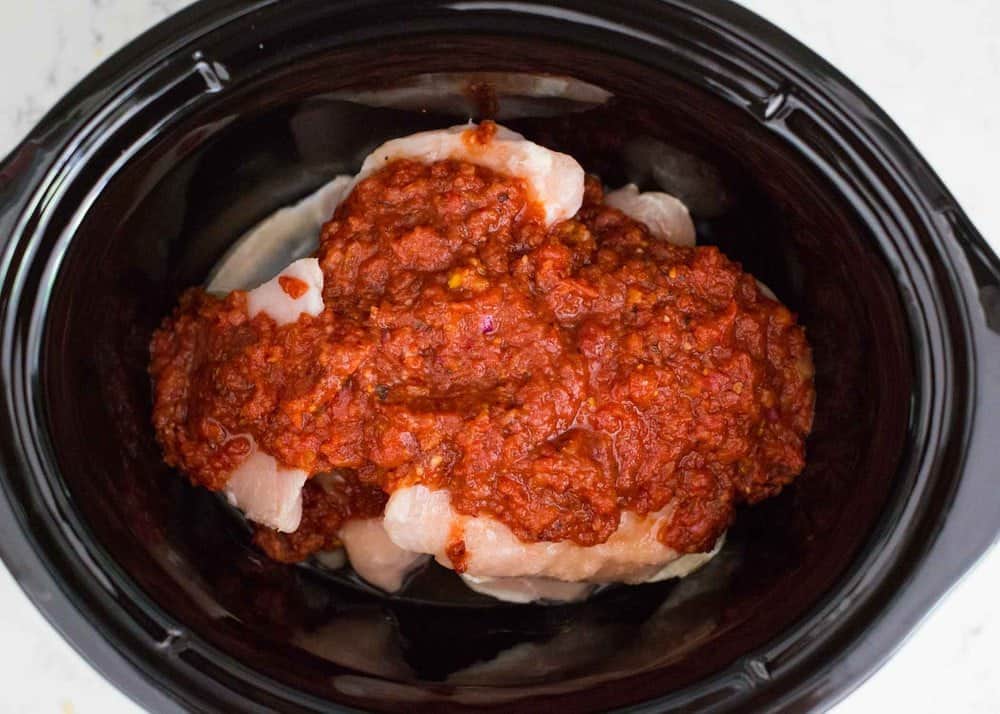 Chicken in crockpot with tinga sauce on top.