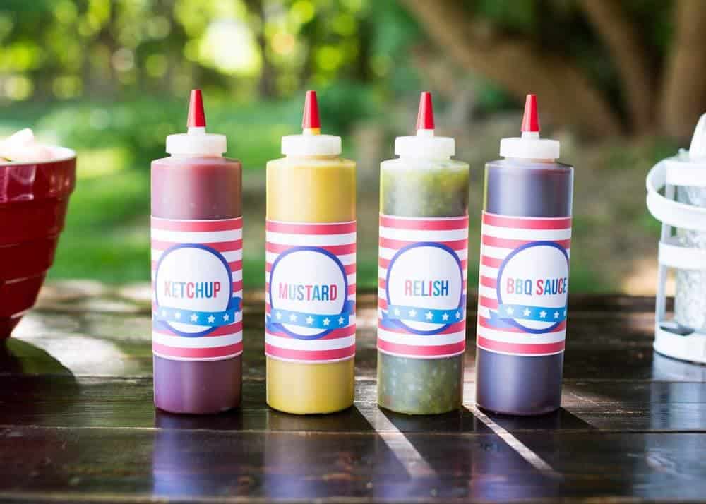 Hot dog bar condiments in squeeze bottles on a table.