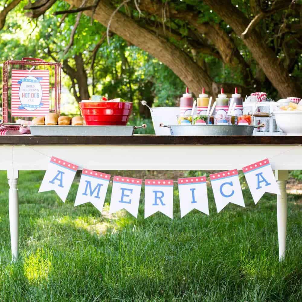 Hot dog bar on a table with an America banner hanging across.