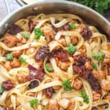 lemon chicken fettuccine in a skillet with sun dried tomatoes and fresh parsley