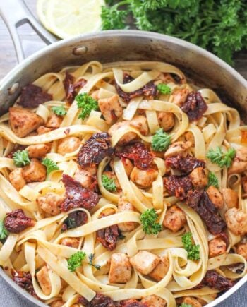 lemon chicken fettuccine in a skillet with sun dried tomatoes and fresh parsley