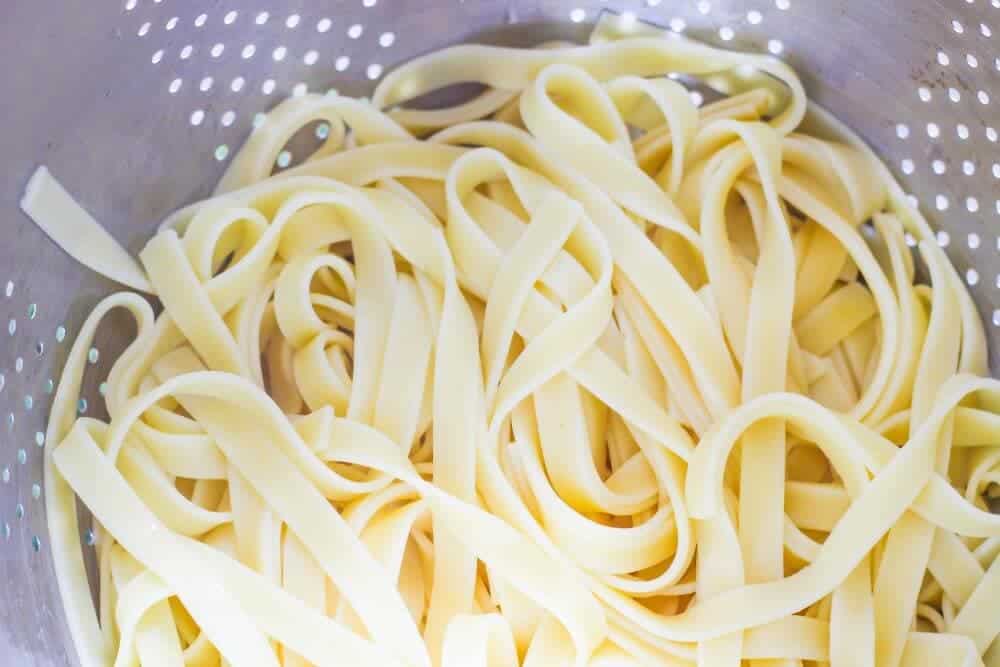 Cooked fettuccine noodles in a strainer.