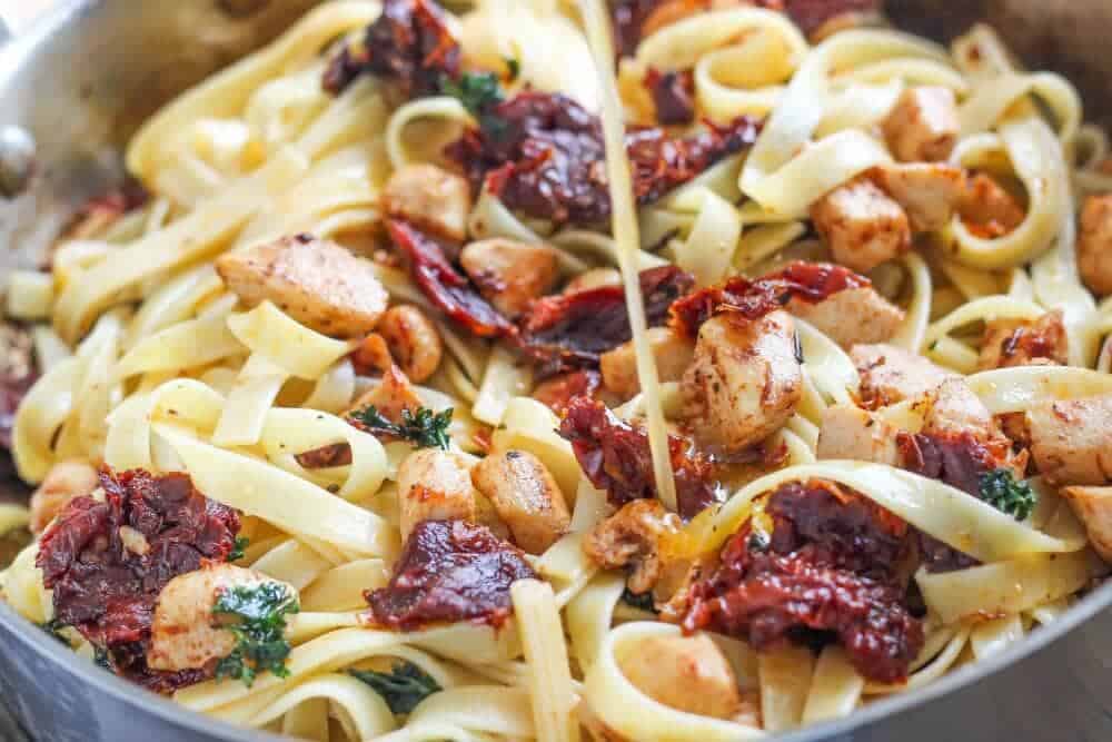 Pouring lemon dressing into fettuccine.