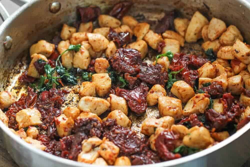 Diced chicken in a pan with sun dried tomatoes and parsley.